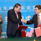 Two men in the foreground shaking hands with two men flanking them behind and sign in Chinese as background