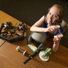 Woman staring through an optical device looking up at the camera, with various devices on the table