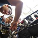 Three students adjust gears on a racecar frame that they designed