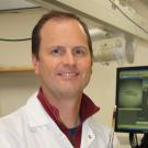 Doug Rowland in lab coat, standing next to imaging monitor