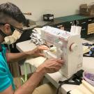 A man in face mask, works at sewing machine, making face masks.