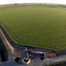 Green farm field bordered by irrigation canal, water pump and divided highway.