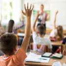 rear view of kids in classroom raising hands 