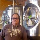 Glen Patrick Fox poses in UC Davis Aggies hoodie, amid brewing equipment.