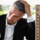 A thermometer in the foreground with a suited man at a computer in the background