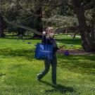 Wioman leaves Quad with a bag of groceries, from an array of bags set 6 feet apart on the Quad.