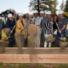 Dignitaries in hard hats, shoveling dirt into the air.