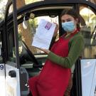 Woman wearing face covering holds food as she steps into electric cart.