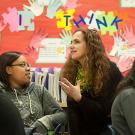 Woman in a high school classroom talking to a student.