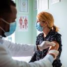 Man administers vaccintaion to woman. Both are wearing masks.