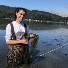 A female student in waders stands in water with eel grass