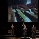 Actors stand before microphones, on stage.