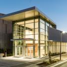 Building exterior in the evening, with lights shining from inside glass-walled lobby 