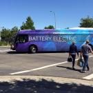 Two people walk through a crosswalk as an electric bus drives by.