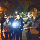 Photo: Police officer surrounded by students, at night, with flashlights, taking notes.