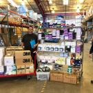 Two men stand amid stacks of supplies.