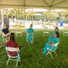 Dean in polo shirt chats with five woman in scrubs under a tent.