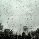 landscape of UC Davis water tower as seen through rain-splattered window on a gray day with above a silhouette of trees.