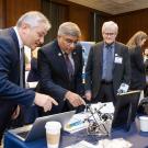 Three men in dark suits looking at gadgets on a table. 