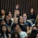 Surrounded by other students, a student raises her hand in class