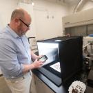 Bearded man using an app to take images of coffee beans inside a lab imaging device