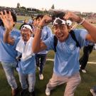 Young people in light-blue shirts cheering exuberantly on a sunny football field