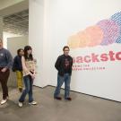 Visitors walking past a colorful exhibition wall labeled "Backstory" in a gallery.