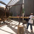 Outdoor scene: man swinging mallet at large bronze sculpture while crowd watches under awning