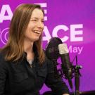 Smiling woman speaking into microphone in purple podcast studio (photo)