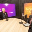 Two men sitting across from each other at a round table, microphones in front of them.