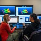 Two women engaged in discussion at computers displaying colorful 3D graphics. UC Davis students Jasmin Baptista and Kaia Broomell examine LiDAR data collected from an orchard canopy as part of a course in Unmanned Aerial Systems.  