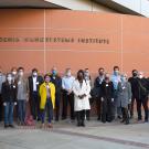 Group of people standing outdoors in front of an orange wall 