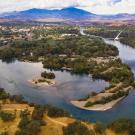 Aerial photo of meandering Sacramento River with tree-covered islands and distant mountains and white sundial bridge