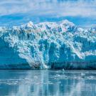 Blue glacier wall with snow-capped peaks reflecting on calm icy water