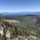 View from rocky slope over pine forests to a blue Lake Tahoe and distant peaks