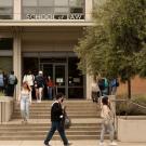 Students walk out of a tree-lined brick building with the words "School of Law" over the door.