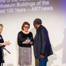 Mike Henderson stands on stage to accept a glass award that reads "Manetti Shrem Museum." Mary Croughan and Rachel Teagle stand opposite Henderson and present the award to him.