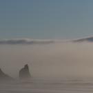 Foggy coastal scene with towering cliff and distant sea stack, muted dawn light