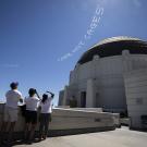 Three people on Griffith Observatory terrace pointing at skywriting over the dome