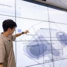 A person points at a large digital display showing data visuals in a modern workspace.