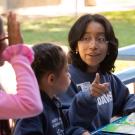 A woman points to the page of a book as two children look on