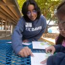 A woman points to the page of a book as two children look on