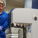 Smiling lab worker in blue coat beside machine decorated with googly eye and paper teeth, photo