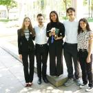 Six students in casual clothing standing by a courtyard fountain, smiling