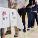 Voters queued at polling booths behind white privacy screens displaying 'VOTE' and small US flags. (Getty)