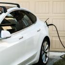 White electric SUV plugged into a home garage charger beside beige garage door