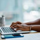 Stock image of a person using a laptop computer. The person's arms and hands are visible. 