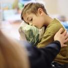 Upset boy hugging pillow on couch while an adult reaches to comfort him.