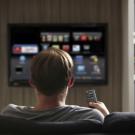The back of a person's head is seen in front of a TV screen with icons on it. 