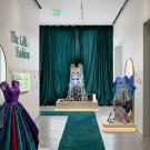 Gallery with mannequins in iridescent gowns, large mirrors, teal runner, and emerald curtains.